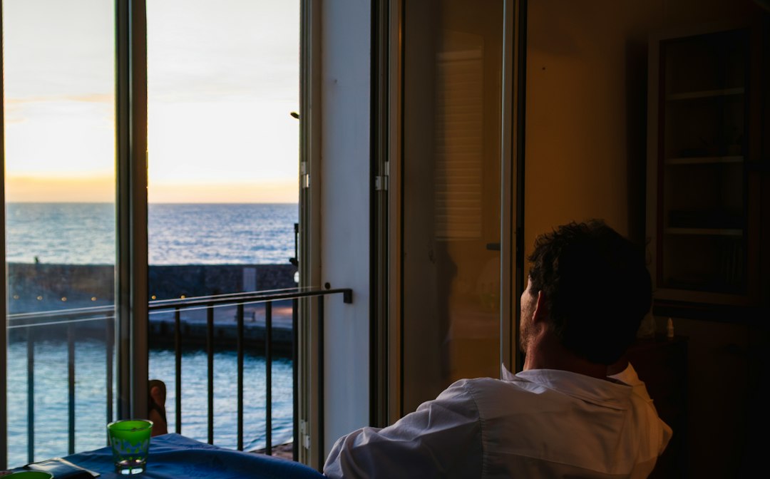 Travel advisor curating bespoke luxury vacation itinerary on laptop overlooking ocean balcony